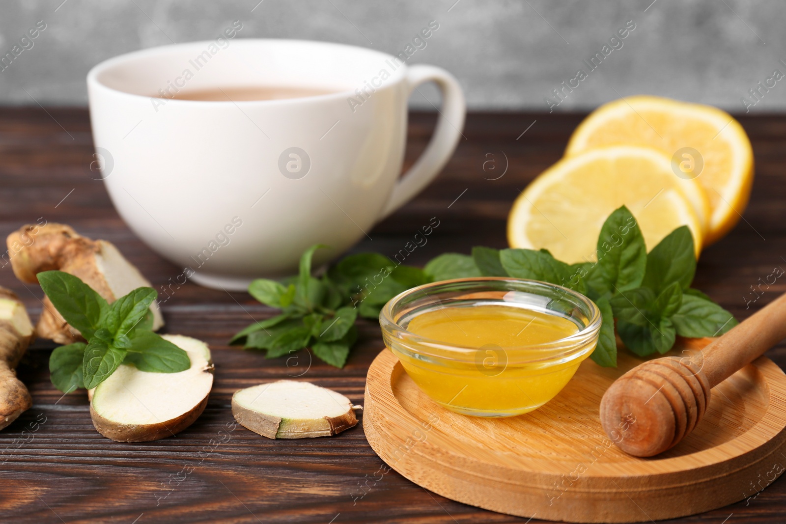 Photo of Bowl with honey for tea, lemon, mint and ginger on wooden table