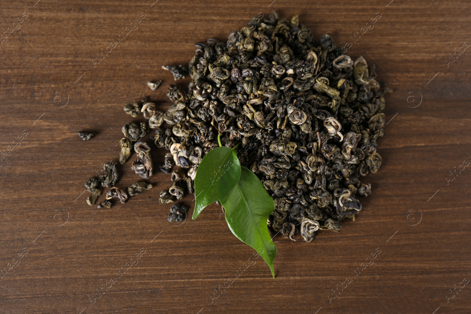 Photo of Heap of dried green tea leaves on wooden table, top view