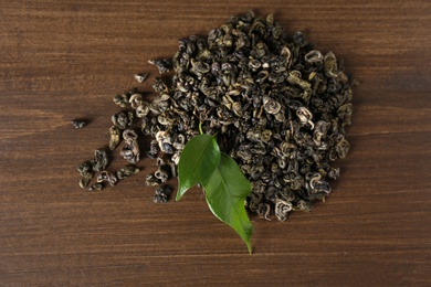 Photo of Heap of dried green tea leaves on wooden table, top view