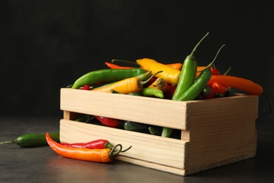 Photo of Wooden crate with different chili peppers on grey table