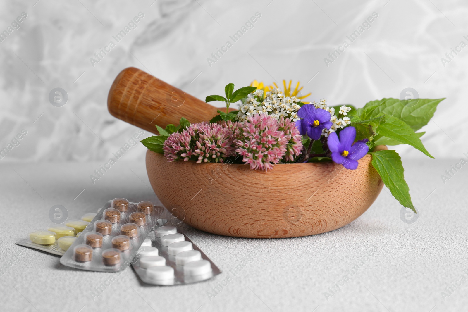 Photo of Wooden mortar with fresh herbs, flowers and pills on white table