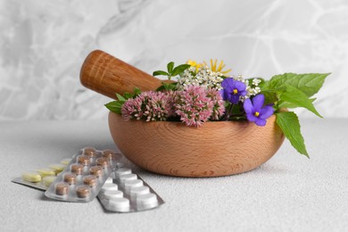 Photo of Wooden mortar with fresh herbs, flowers and pills on white table