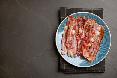 Photo of Slices of tasty fried bacon on dark table, top view. Space for text