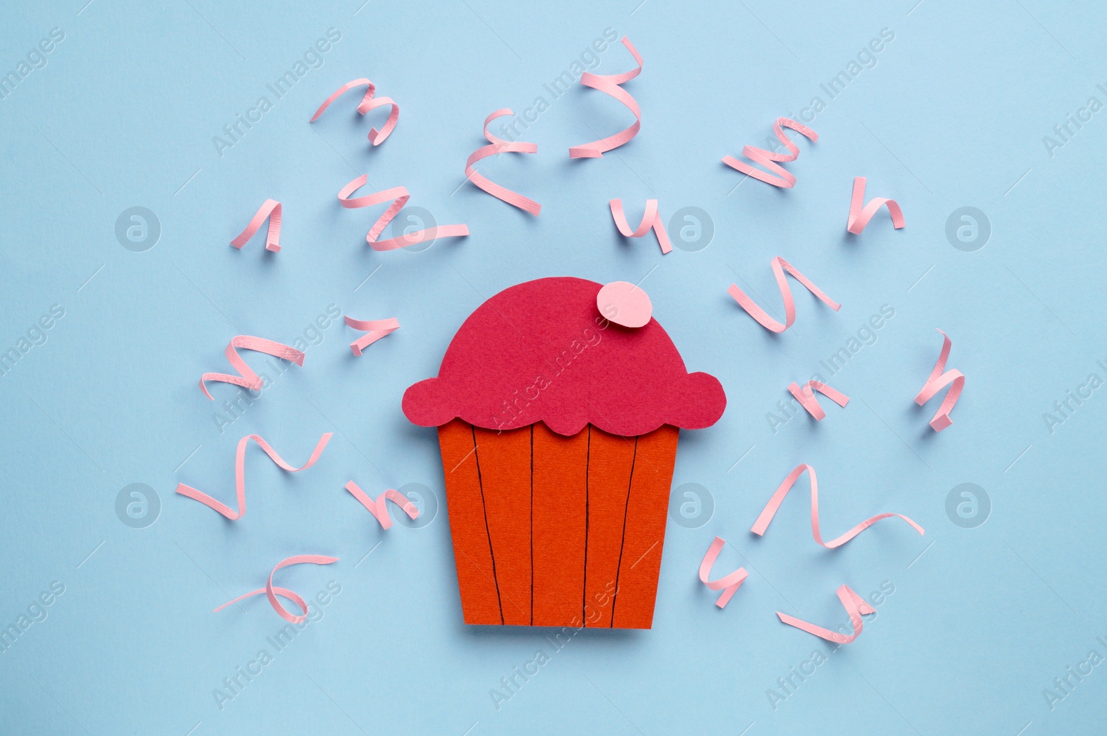 Photo of Birthday party. Paper cupcake surrounded by serpentine streamers on light blue background, top view
