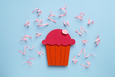 Photo of Birthday party. Paper cupcake surrounded by serpentine streamers on light blue background, top view