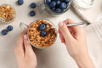 Photo of Woman eating granola with blueberries on grey marble table, top view