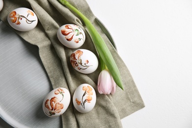 Photo of Beautifully painted Easter eggs and tulip on white table, space for text