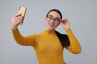 Smiling young woman taking selfie with smartphone on grey background