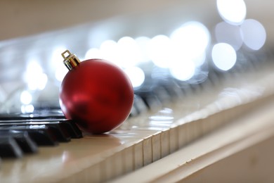 Beautiful red bauble and fairy lights on piano keys, space for text. Christmas music