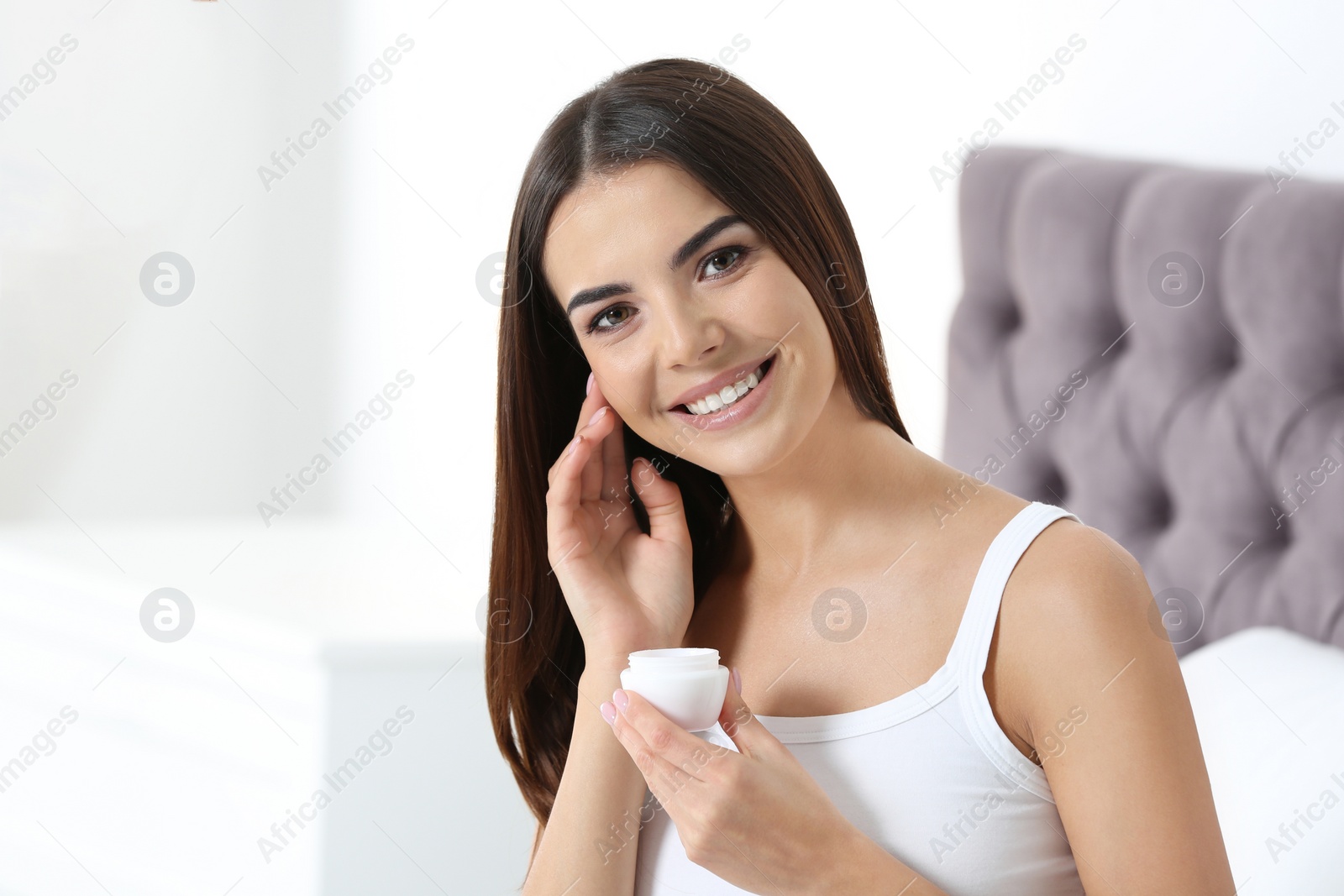 Photo of Young woman with jar of cream in bedroom. Beauty and body care