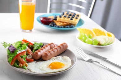 Delicious breakfast with fried egg and sausages served on white table