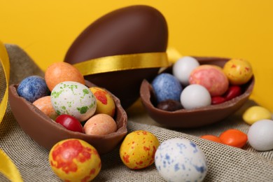 Photo of Whole and halves of chocolate eggs with colorful candies on cloth, closeup