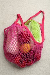 Fresh Chinese cabbage and other products in string bag on light textured table, top view