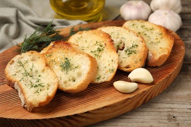 Tasty baguette with garlic, dill and oil on wooden table, closeup