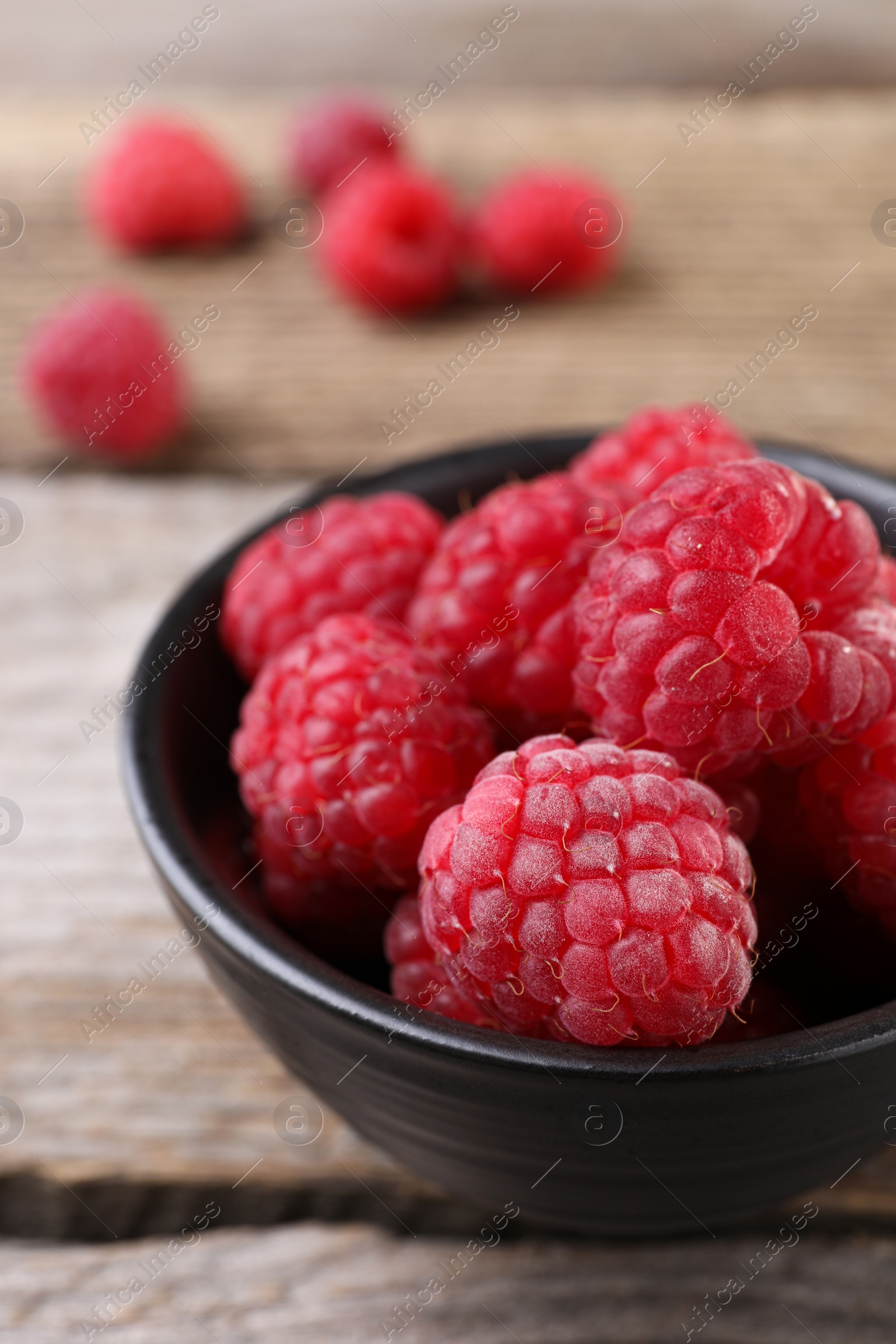 Photo of Tasty ripe raspberries in bowl on wooden table, closeup