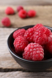 Tasty ripe raspberries in bowl on wooden table, closeup