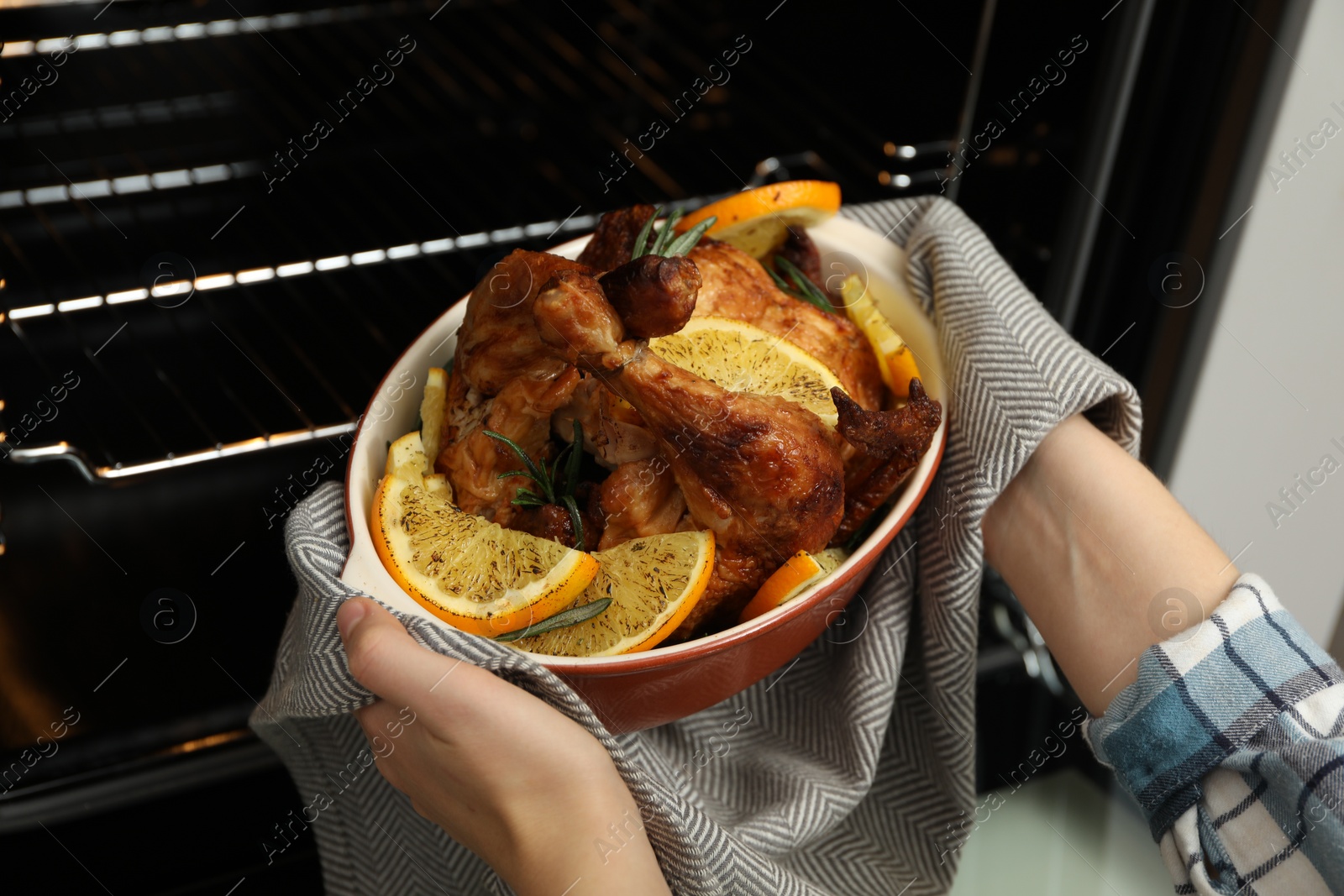 Photo of Woman taking baked chicken with orange slices out of oven, closeup