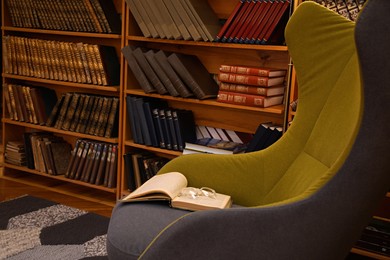 Photo of Comfortable armchair with book and glasses in cozy home library