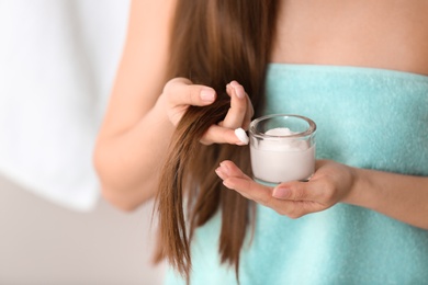 Photo of Woman holding glass bowl with hair mask on blurred background, closeup. Split ends