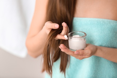 Woman holding glass bowl with hair mask on blurred background, closeup. Split ends