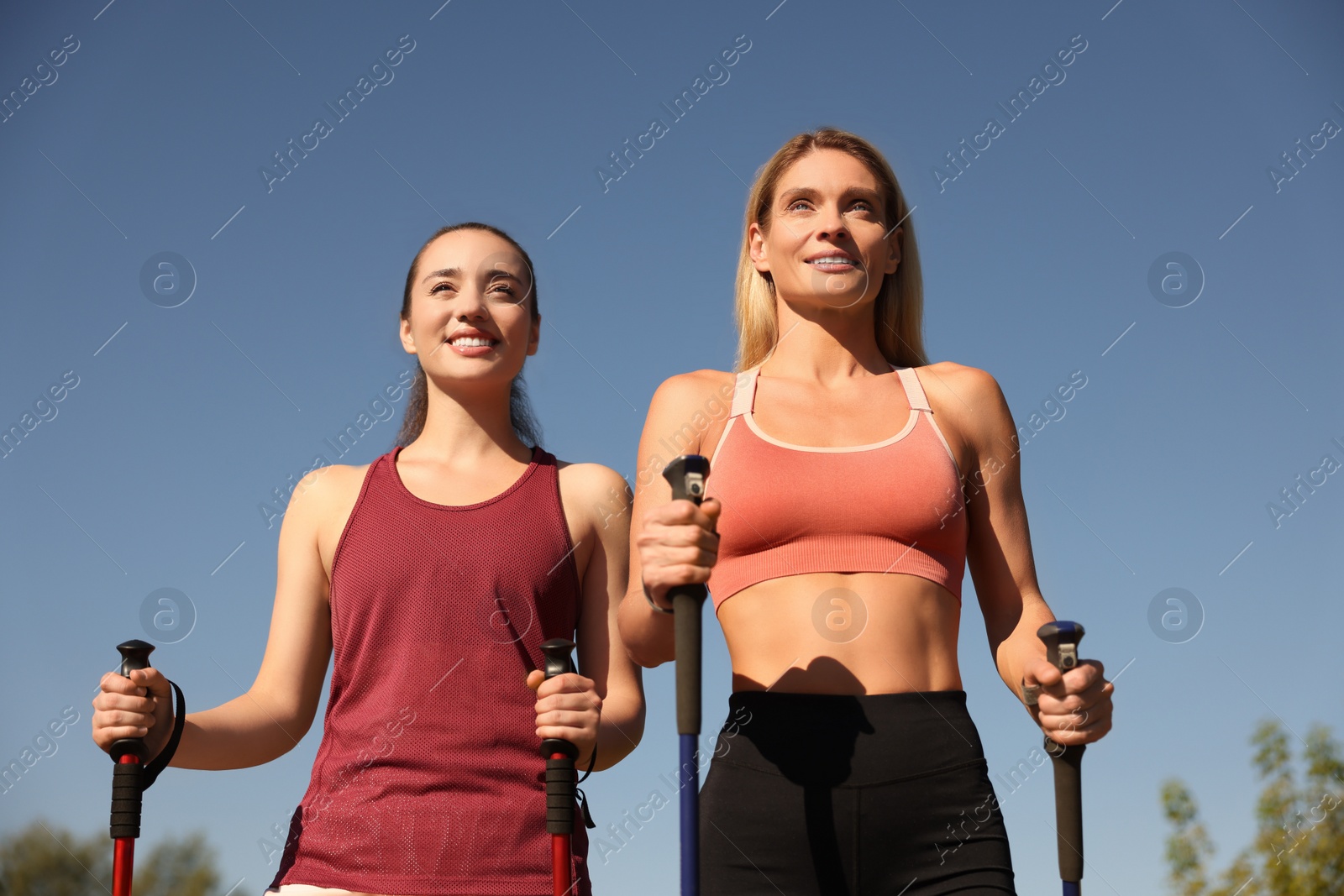 Photo of Happy women practicing Nordic walking with poles outdoors, low angle view