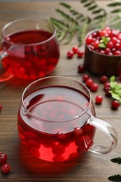 Photo of Tasty hot cranberry tea in glass and fresh berries on wooden table