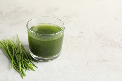 Photo of Wheat grass drink in glass and fresh sprouts on light table. Space for text