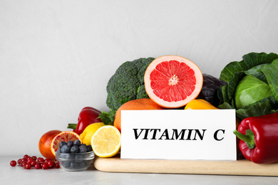 Photo of Paper note with phrase VITAMIN C and fresh products on light table