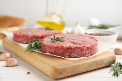 Photo of Raw hamburger patties with rosemary on white wooden table, closeup