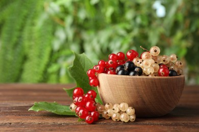 Photo of Different fresh ripe currants and green leaves on wooden table outdoors, space for text