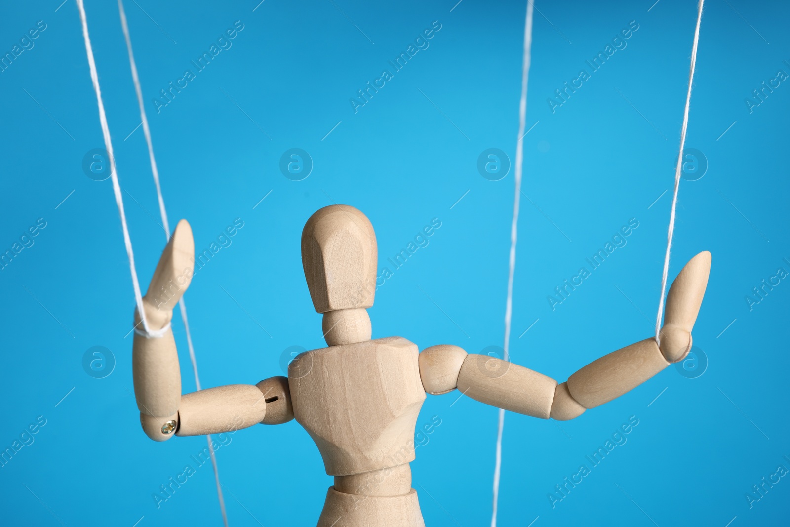 Photo of One wooden puppet with strings on light blue background