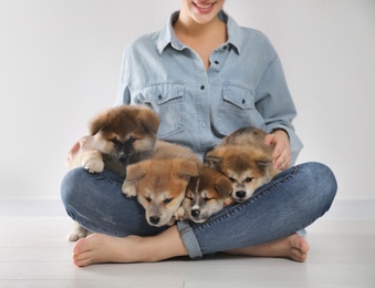 Photo of Woman with Akita Inu puppies sitting on floor near light wall, closeup
