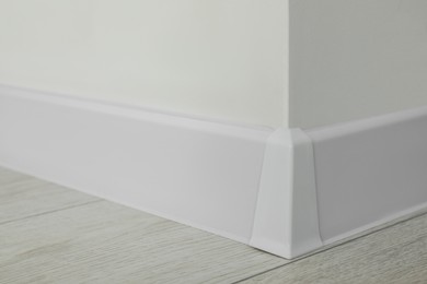 White plinth with connector on laminated floor near wall indoors, closeup