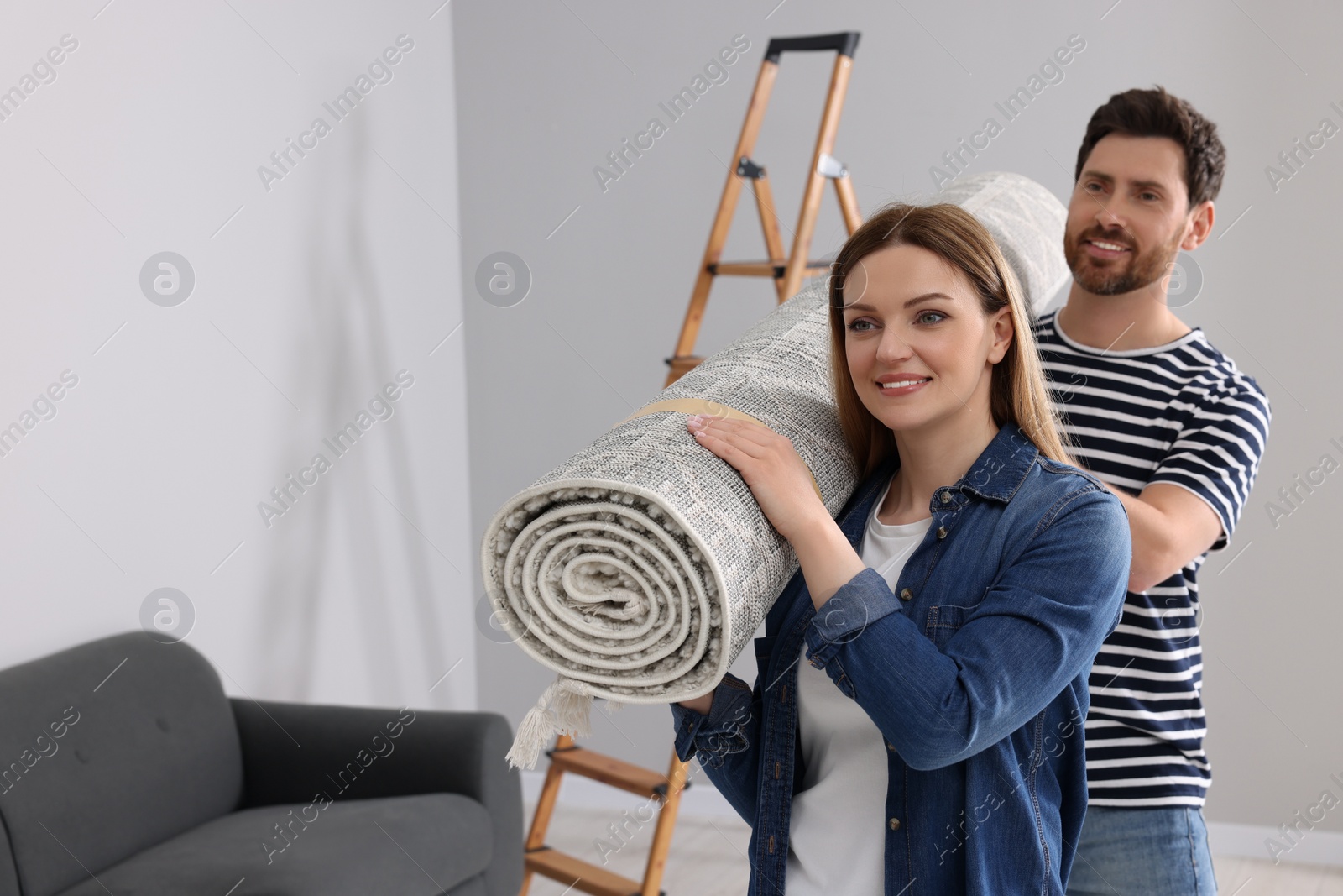 Photo of Smiling couple holding rolled carpet in room, space for text