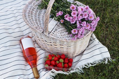 Photo of Picnic basket, flowers, bottle of wine and strawberries on blanket outdoors