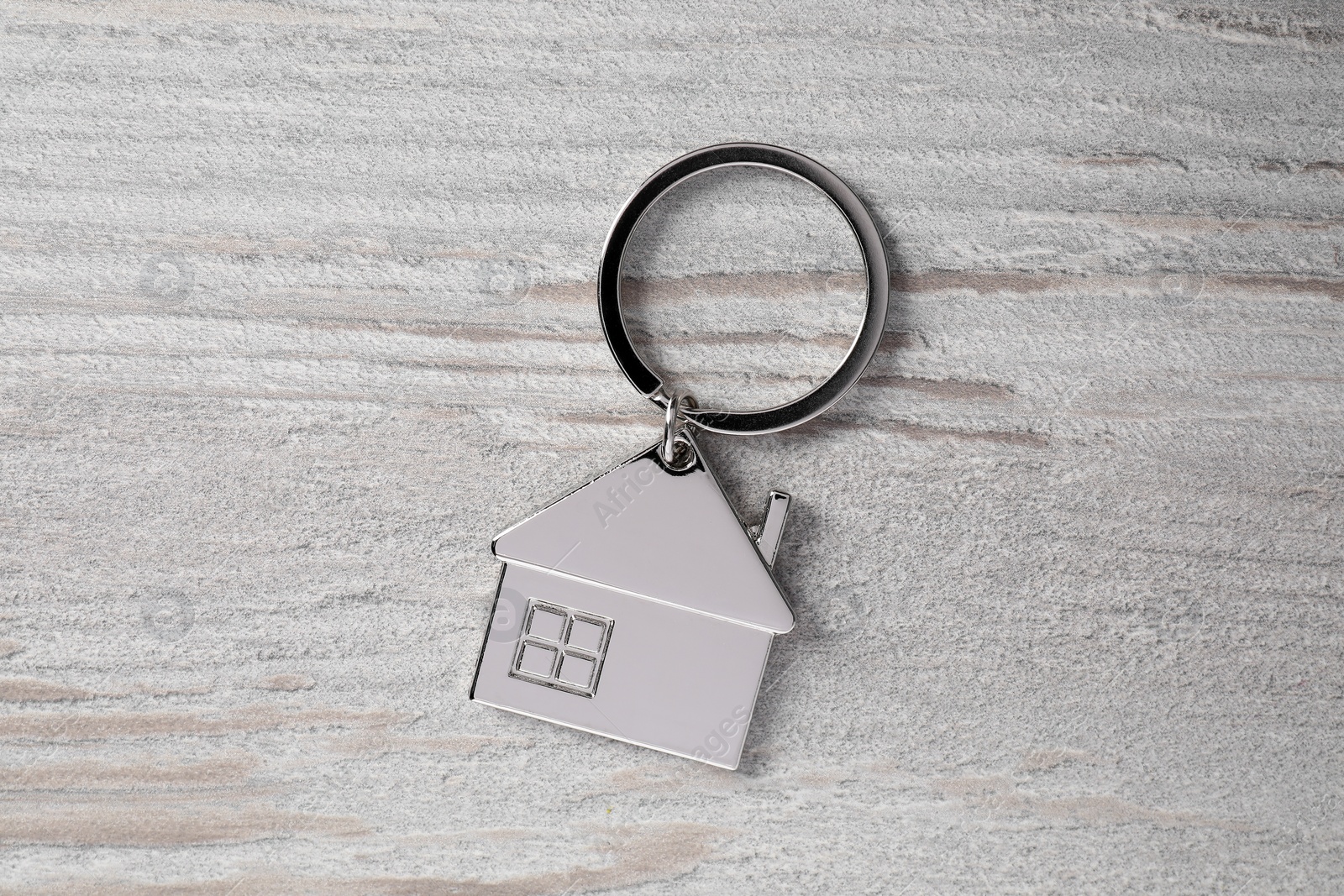 Photo of Metal keychain in shape of house on light wooden table, top view