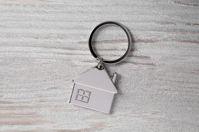 Metal keychain in shape of house on light wooden table, top view