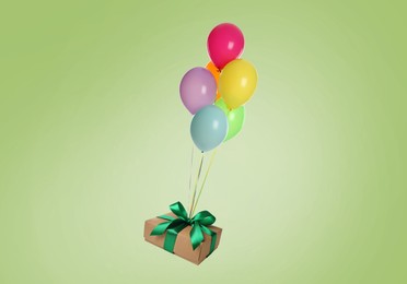 Many balloons tied to gift box on light green background