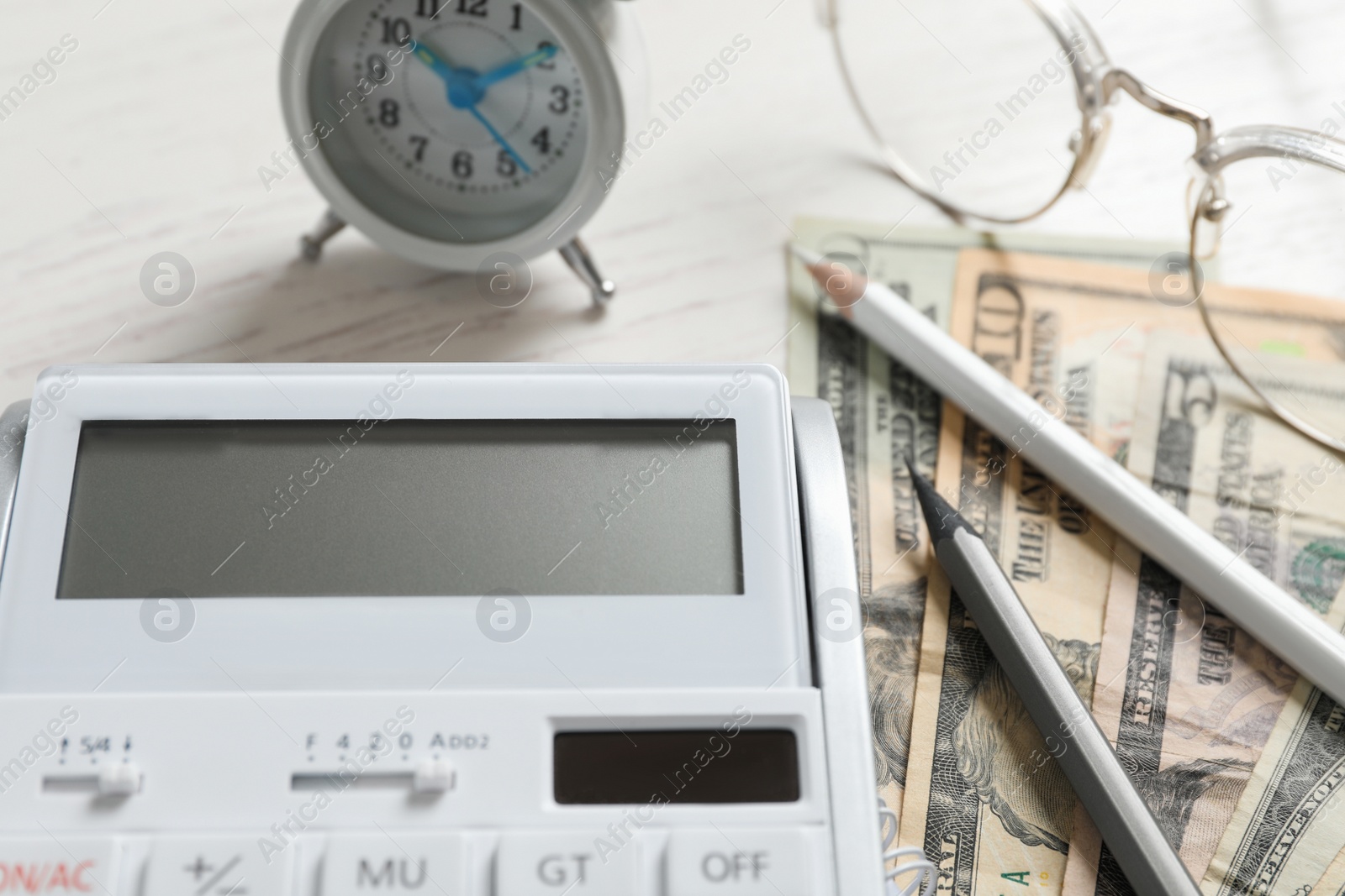 Photo of Calculator, money, pencils and alarm clock on white wooden table, closeup. Tax accounting