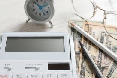 Calculator, money, pencils and alarm clock on white wooden table, closeup. Tax accounting