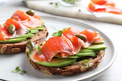 Delicious sandwiches with salmon, avocado and capers on plate, closeup