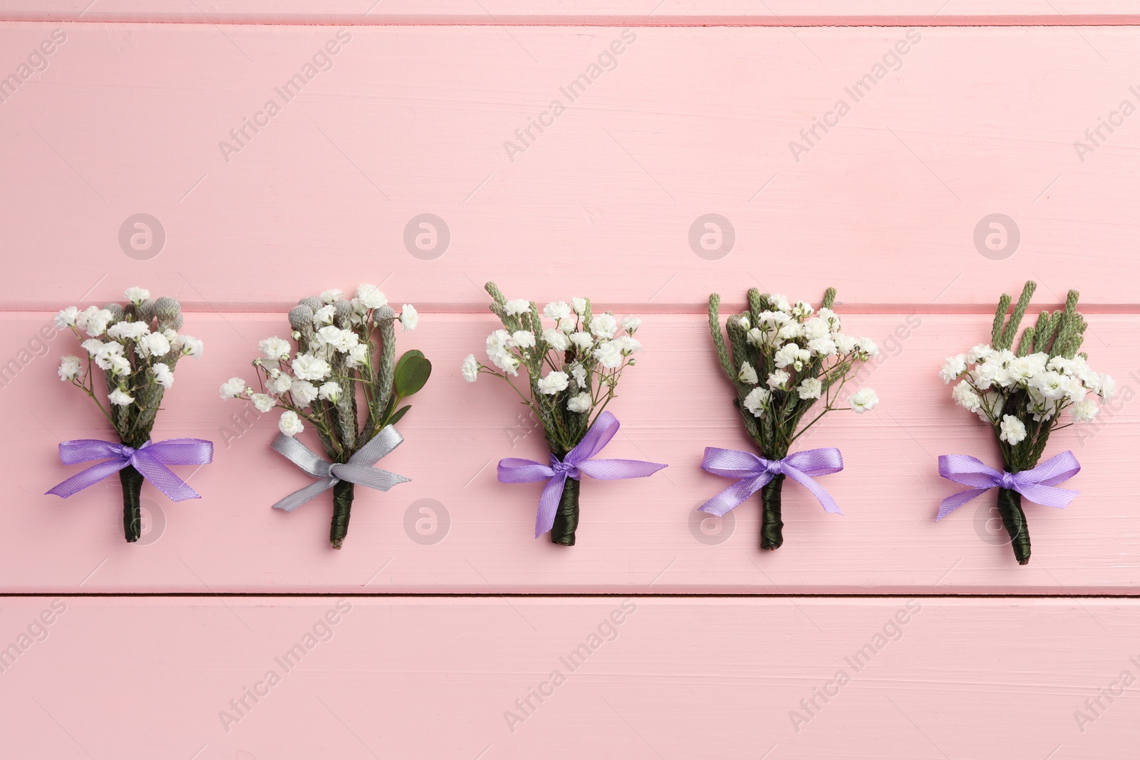 Photo of Many small stylish boutonnieres on pink wooden table, flat lay