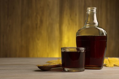 Photo of Tasty maple syrup, spoon and leaves on wooden table. Space for text