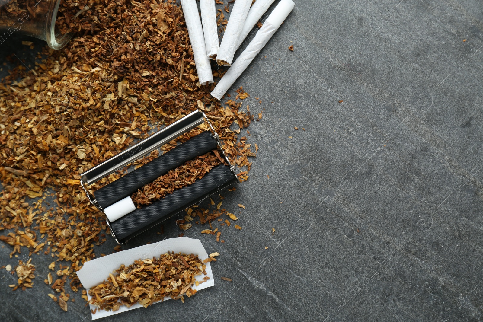 Photo of Flat lay composition with roller and tobacco on dark grey table, space for text. Making hand rolled cigarettes