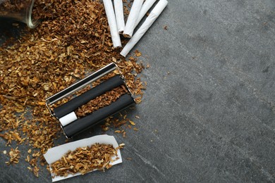 Flat lay composition with roller and tobacco on dark grey table, space for text. Making hand rolled cigarettes