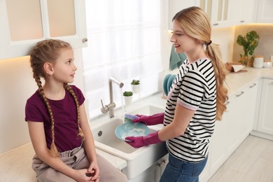 Photo of Mother washing plate while speaking with daughter in kitchen