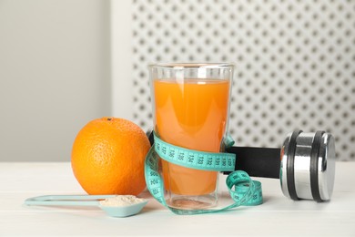 Photo of Tasty shake, orange, dumbbell, measuring tape and powder on white wooden table. Weight loss