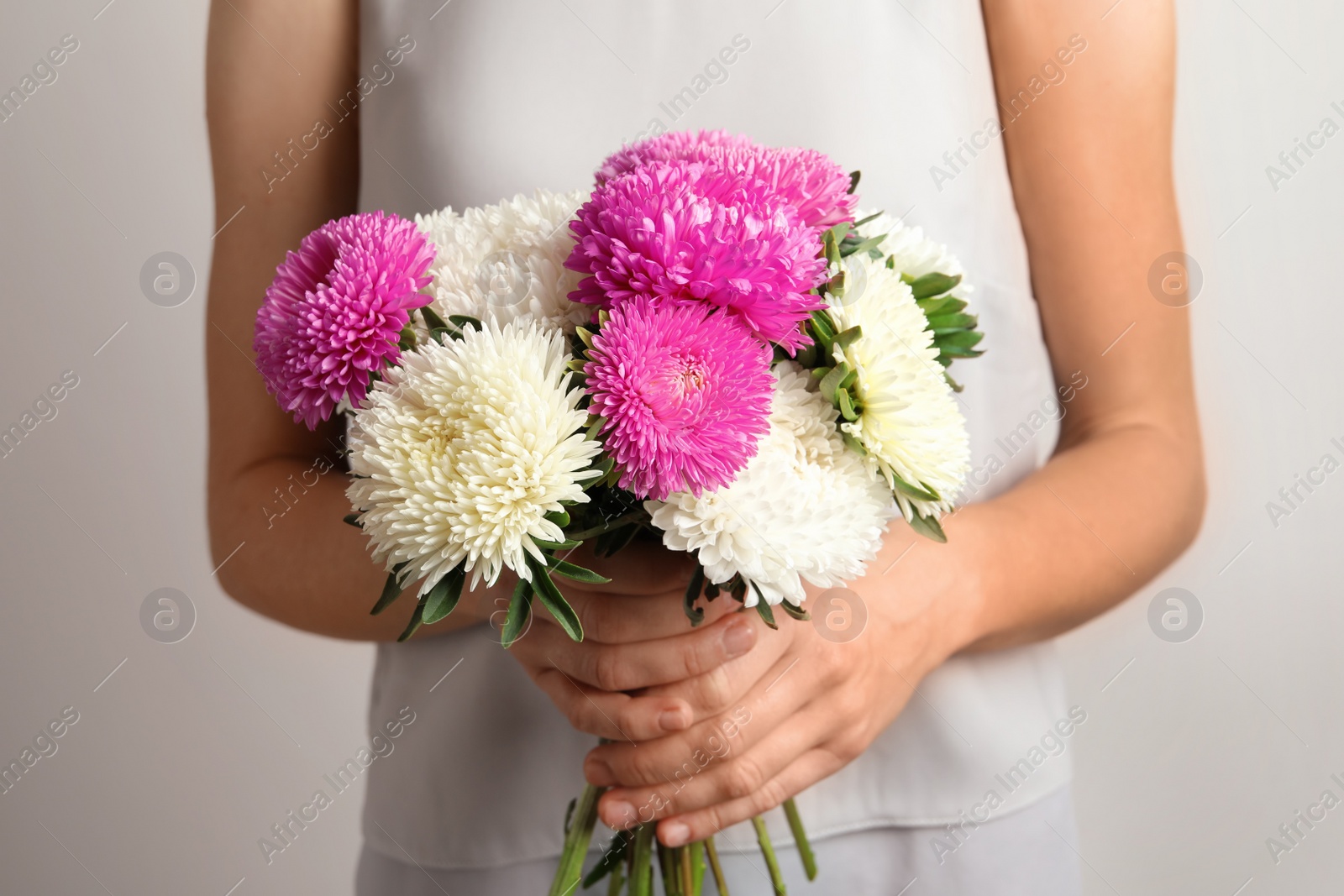 Photo of Woman holding beautiful aster flower bouquet against light background