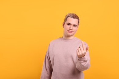 Photo of Handsome man inviting to come in against orange background, space for text