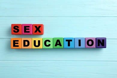 Photo of Colorful wooden blocks with phrase "SEX EDUCATION" on light blue background, flat lay